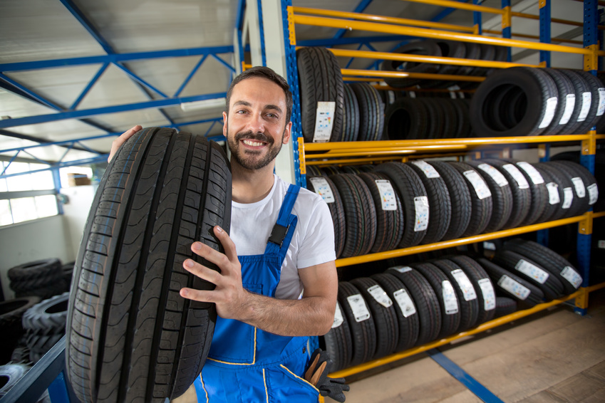 smiling auto mechanic carrying tire Reifen für Geschäftskunden - Pneu Schaller - Lachender Mechaniker mit Reifen